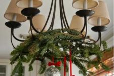a pretty vintage chandelier with lampshades decoraed with evergreens, silver ornaments and red ribbon is a cool and chic idea