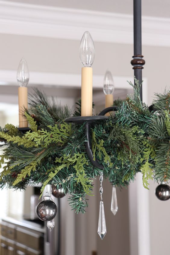 a stylish chandelier with evergreens and crystals plus black ornaments is a cool decoration for the holidays