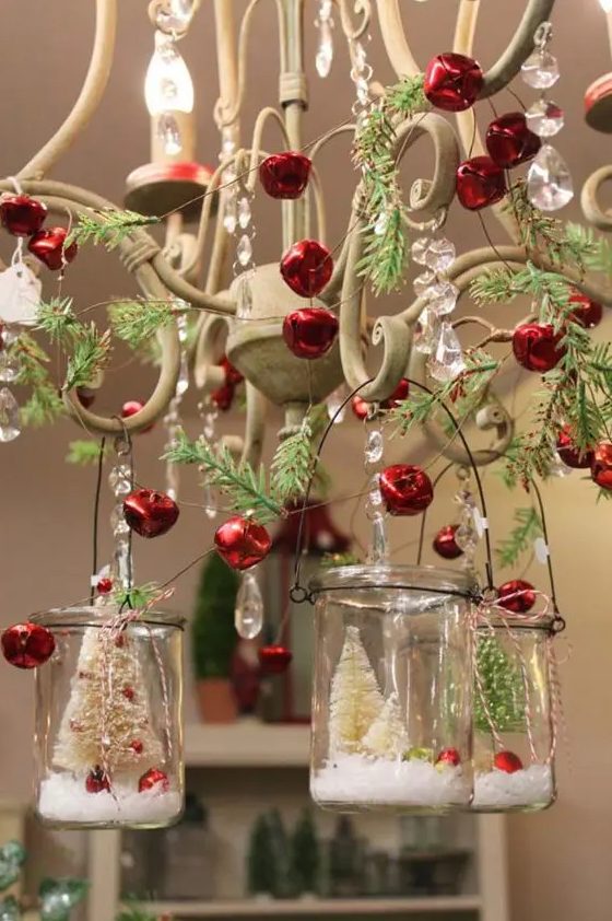 a vintage chandelier decorated with red bells, evergreens and mini terrariums hanging on it is fab