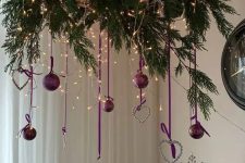 a wreath Christmas chandelier of evergreens, lights, purple ornaments, hearts and snowflakes is amazin