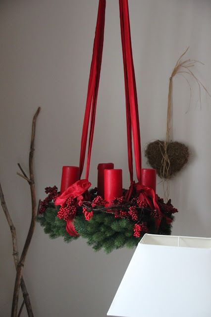 an evergreen wreath as a Christmas chandelier, with red berries, ribbons and red pillar candles