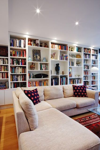 an oversized white bookcase with additional lights take the whole wall turning the living room into a library