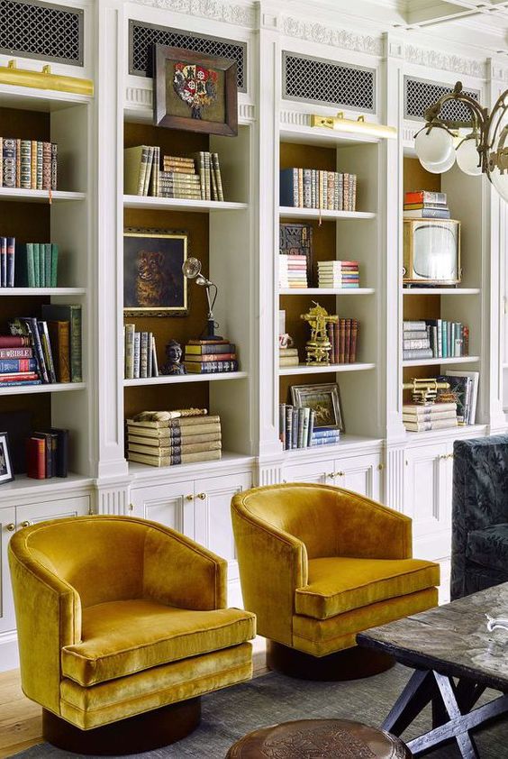 elegant and refined built-in white bookshelves with molding look bold and with bright chairs create a reading space