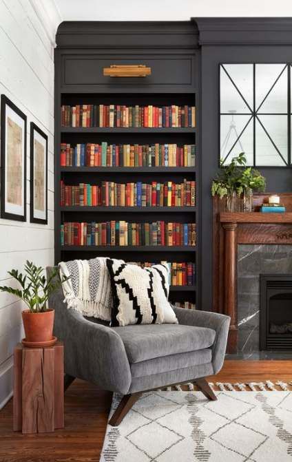graphite grey built in bookcases and a grey chair plus a stone fireplace to create a cozy dark reading nook