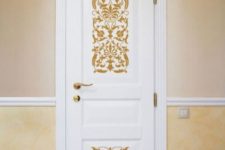 a white door with gold ornate stencils and a gold handle looks very chic and very stylish