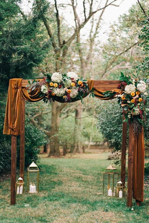 a bright fall wedding arch with mustard velvet, bright and white blooms, foliage and candle lanterns
