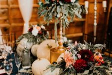 a bright fall wedding centerpiece of white pumpkins, bright flowers on a stand and candles