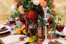 a bright floral wedding centerpiece with rust, orange, creamy blooms and greenery plus burgundy candles