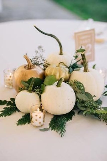 a neutral fall wedding centerpiece of white pumpkins, greenery and candles in polka dot candleholders