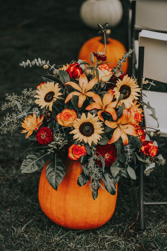 a pumpkin with bright fall blooms and greenery is great for fall wedding decor including lining the aisle