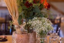 a rustic fall centerpiece of a wood slice, pumpkins, candles, bright blooms, baby’s breath and a wheat bundle