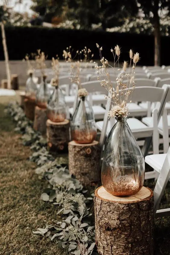 a rustic fall wedding arch with tree stumps, vases with dried grasses and blooms and eucalyptus