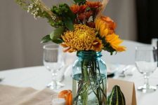 a rustic fall wedding centerpiece of a wood slice, candles, pumpkins and bright fall blooms and wheat in a jar