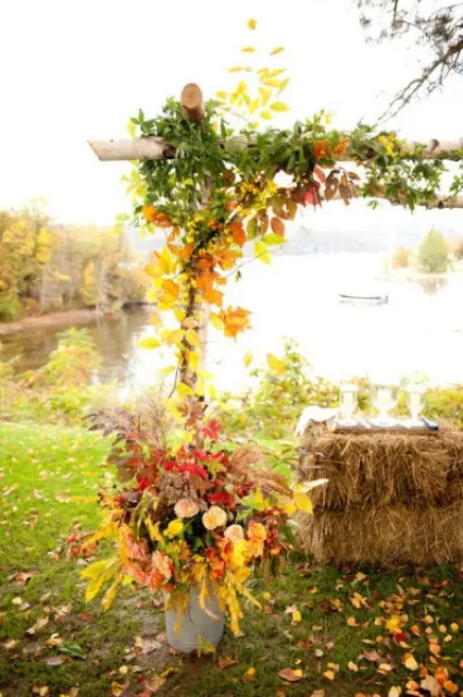 a rustic wedding arch placed in buckets and decorated with bright fall foliage and greenery