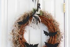 a Halloween wreath with moss and hay, bats, a skeleton hand and leaves for front door decor