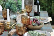 a beautiful outdoor fall tablescape with a plaid tablecloth, amber goblets, driftwood, greenery, gold touches and plates