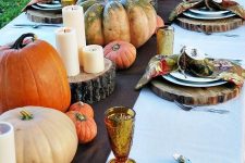 a bold fall table setting with a brown runner, wood slice placemats, natural bright pumpkins and candles and bold napkins