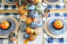 a copper and blue fall tablescape with a striped runner and plaid placemats, blue, metallic and rust pumpkins, leaves and copper glasses