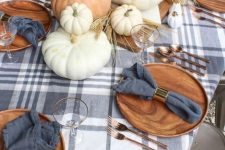 a cozy modern rustic tablescape with a plaid tablecloth, wooden plates, copper cutlery, natural pumpkins and wheat