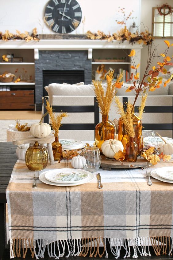 a cozy rustic fall tablescape with plaid linens, printed plates, dried leaves and grasses and neutral pumpkins