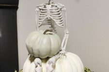 a creative Halloween decoration of a skeleton sitting on pumpkins and some greenery is very stylish