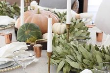 a neutral farmhouse table setting with copper candleholders, brass candleholders, a greenery runner and natural pumpkins