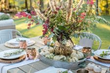 a relaxed natural tablescape with wood slices as placemats, a lush leaf, grass and berry arrangement and copper mugs