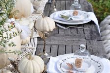 a relaxed outdoor fall tablescape with a macrame runner, white pumpkins and blooms, white plates and napkins
