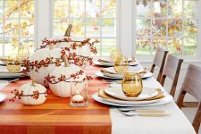 a simple and bright fall table setting with a striped runner, white pumpkins with berries, candles and stained glasses