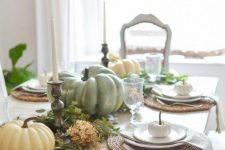 a simple rustic fall tablescape with a greenery and dried bloom runner, natural pumpkins and candles and woven placemats