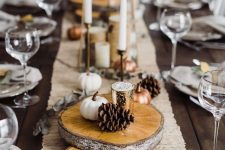 a stylish fall table setting with a burlap runner, wood slices, pinecones, mini faux pumpkins, thin candles