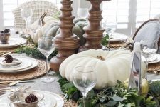 a stylish neutral fall tablescape with greenery and natural pumpkins, candles in wooden candleholders, woven placemats and pinecones