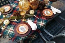 a woodland fall table setting with a bright plaid runner, metallic chargers, antlers, moss, pinecones and bright fall leaves