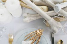 an elegant white Halloween table setting with bones, gilded skeleton hands, cutlery and white spiders