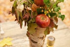 a natural fall centerpiece of a tree stump, apples, greenery, berries and white blooms plus pinecones is a super cool
