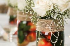 a pretty fall wedding or party centerpiece of apples in a jar, foliage, baby’s breath, white roses and burlap