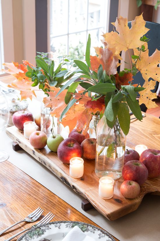 a rustic fall centerpiece of a wooden board with apples, candles, foliage and fall leaves in vases is easy to make
