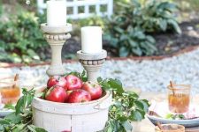a wooden basket with red apples and lush foliage, a couple of candles in wooden candleholders for a fall centerpiece