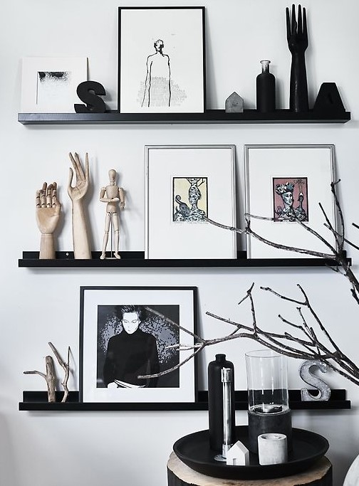 a Nordic gallery wall with black ledges contrasting the white wall, bold art, statuettes and monograms plus branches