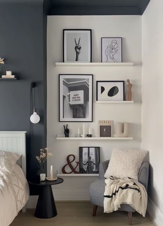a Scandinavian bedroom with a black accent wall, a ledge gallery wall with art and decor, a grey chair with a pillow and a blanket