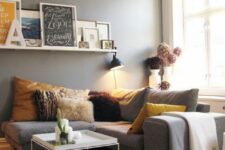 a Scandinavian living room with grey walls, a grey sectional, bold pillows, a coffee table, a ledge with artwork