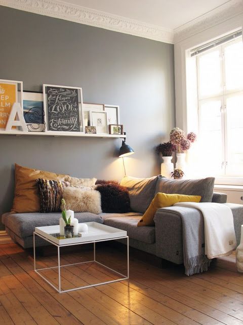 a Scandinavian living room with grey walls, a grey sectional, bold pillows, a coffee table, a ledge with artwork