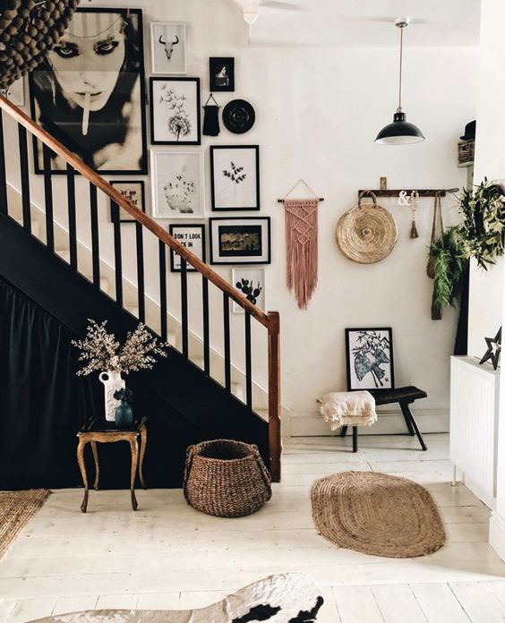 a black and white entryway with a black and white gallery wall over the stairs, macrame, some jute decor and greenery around
