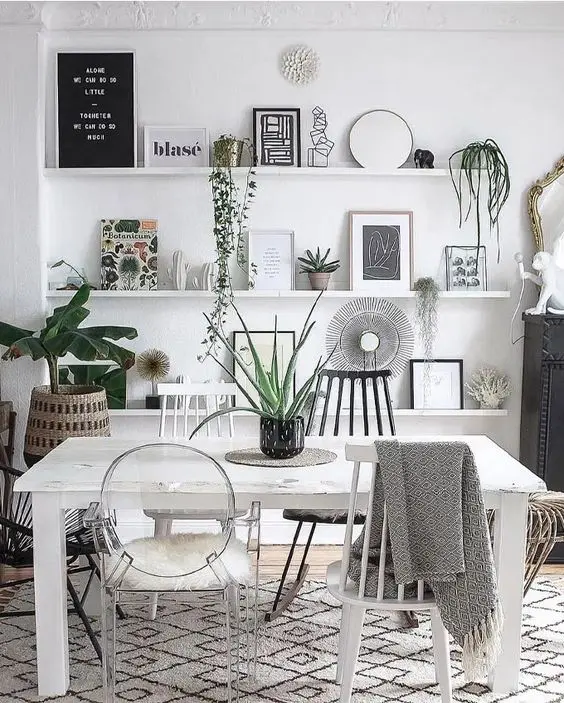 a boho Scandinavian living room with ledges with artwork, potted plants and mirrors, a white table and mismatching chairs