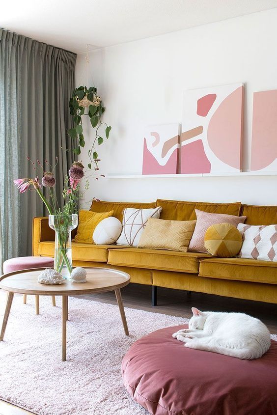 a bold and catchy living room with a mustard sofa, a mauve pouf, a coffee table, a ledge with artwork and green curtains