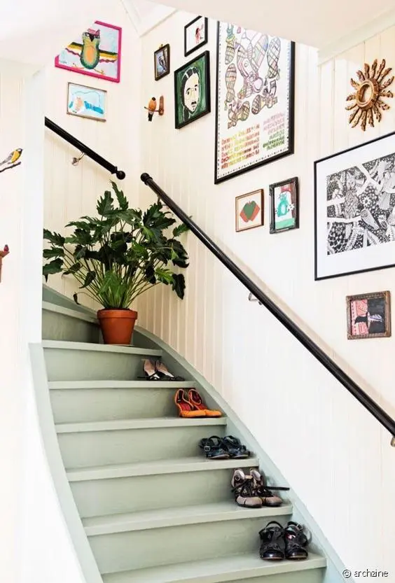 a bright and eclectic gallery wall with lots of fun art in mismatching frames is a cool idea for staircase decor