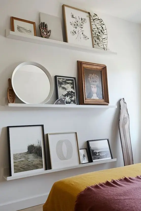 a chic contemporary gallery wall with white ledges, various artworks, a round mirror, some figurines and a greenery branch