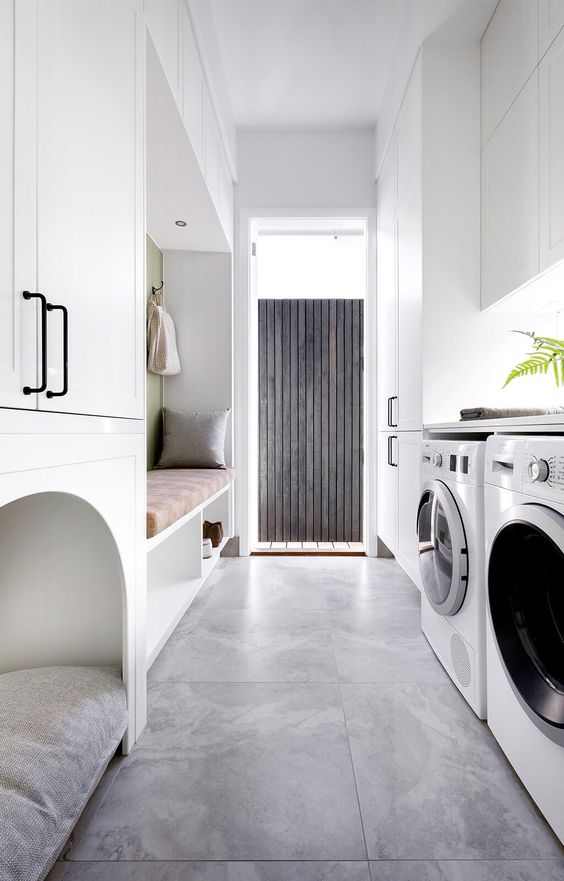 a contemporary laundry mudroom with sleek white cabinets, a bench with storage, a pet bed and built-in appliances