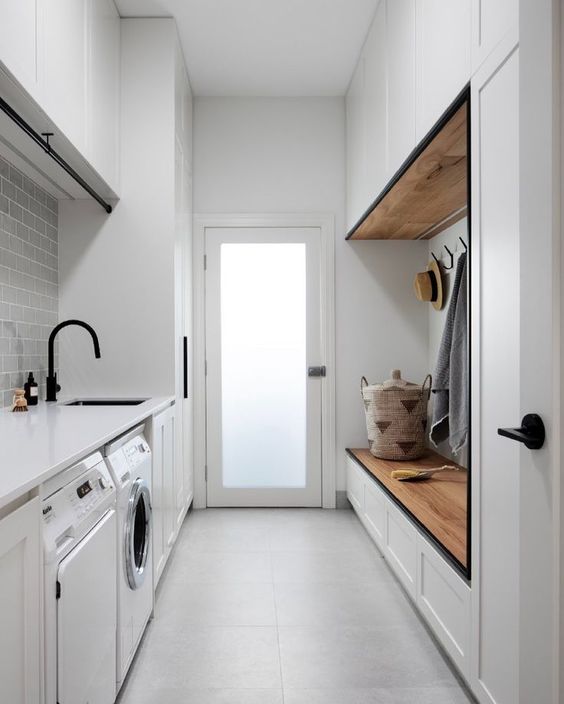a cool contemporary mudroom laundry with sleek cabinets, a stained bench, built-in appliances and cabinets plus black fixtures