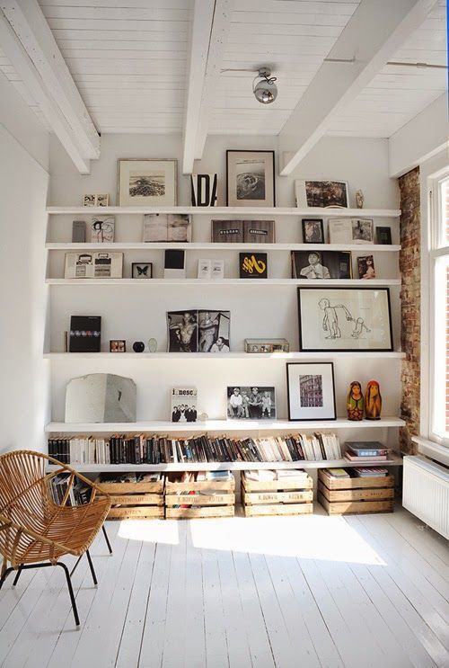 a cozy nook with white ledges, black and white artwork and books, crates with books and a rattan chair
